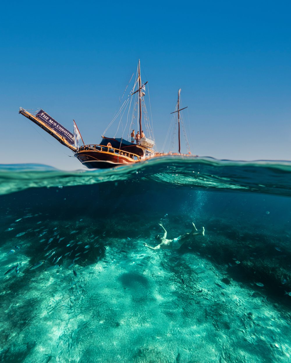 Half underwater shot of a swimmer below a traditional sailing boat in the Ionian sea