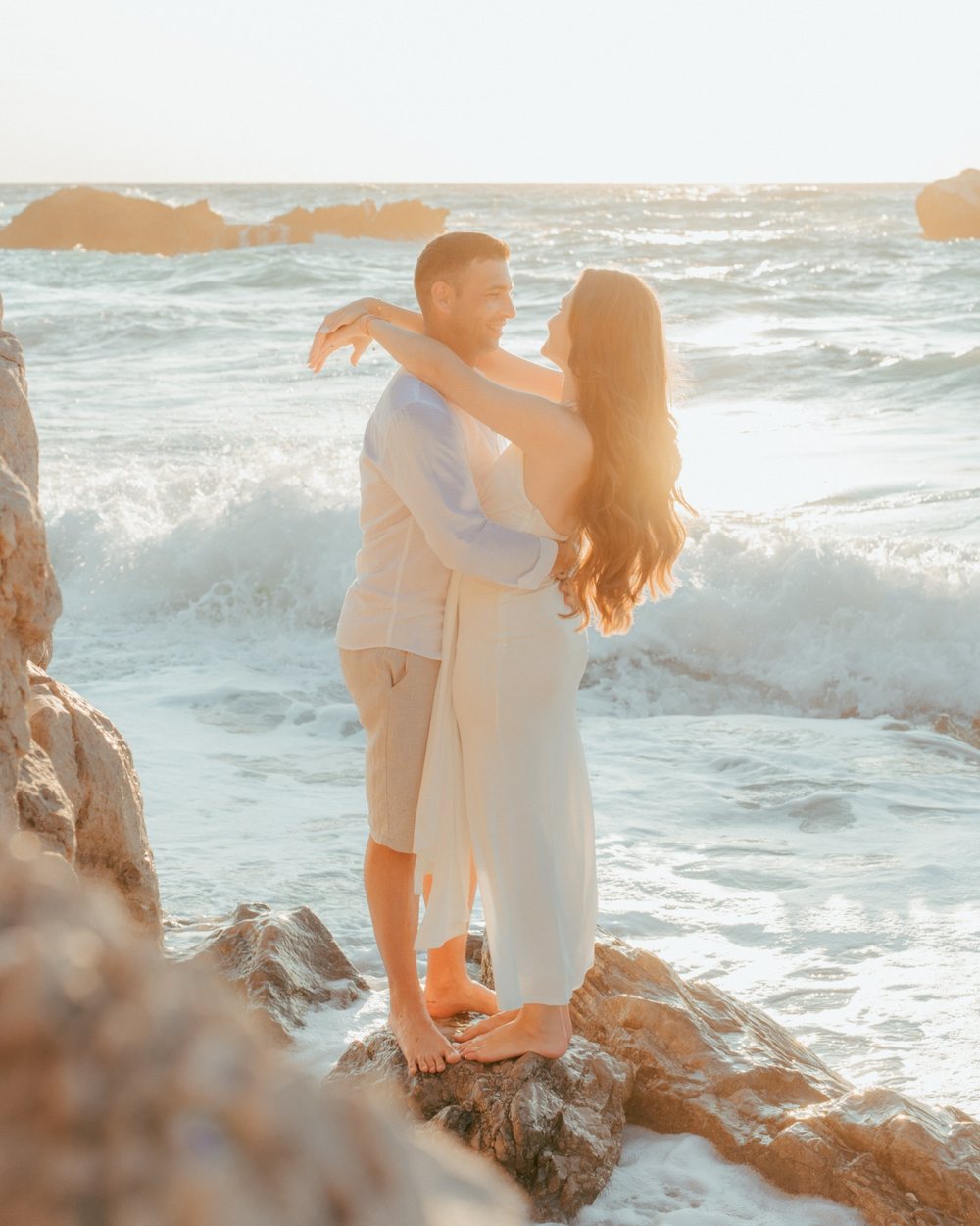Couple embracing on the rocks as waves break in Lefkada